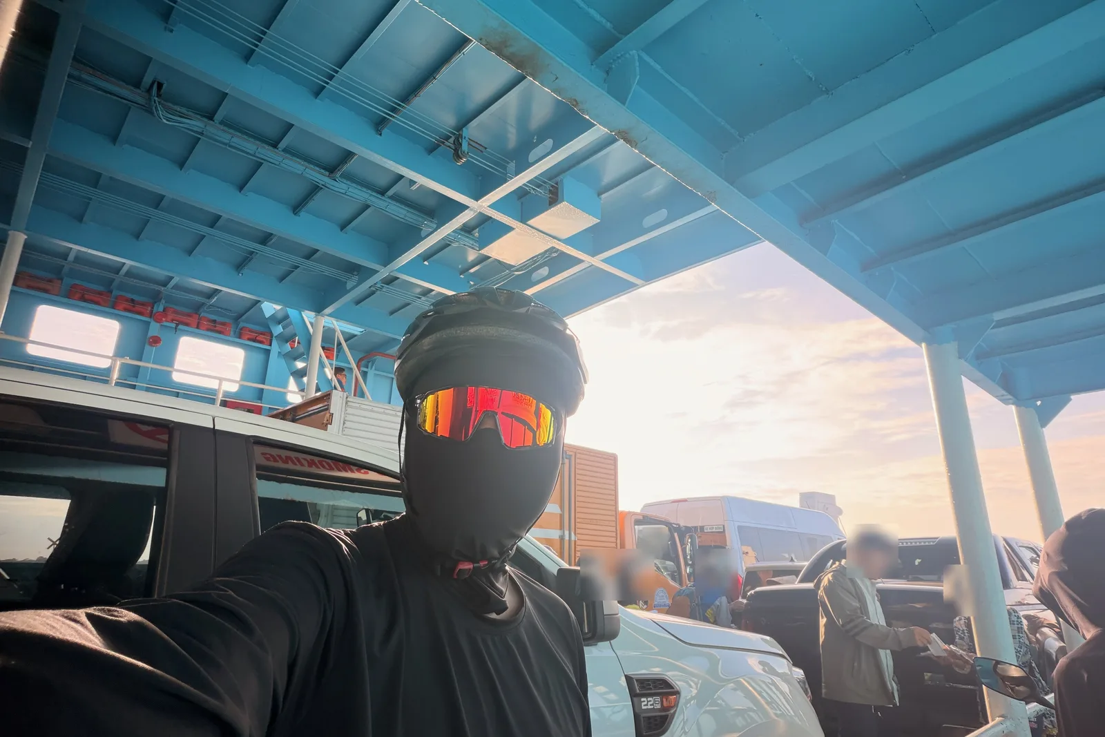 Inside a blue steel vehicle ferry at sunrise, packed with cars, vans and motorbikes, with low sun coming through the open side