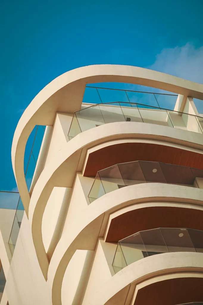 Looking upward at white curved concrete arcs and brows layered over glass balustrades and warm timber soffits